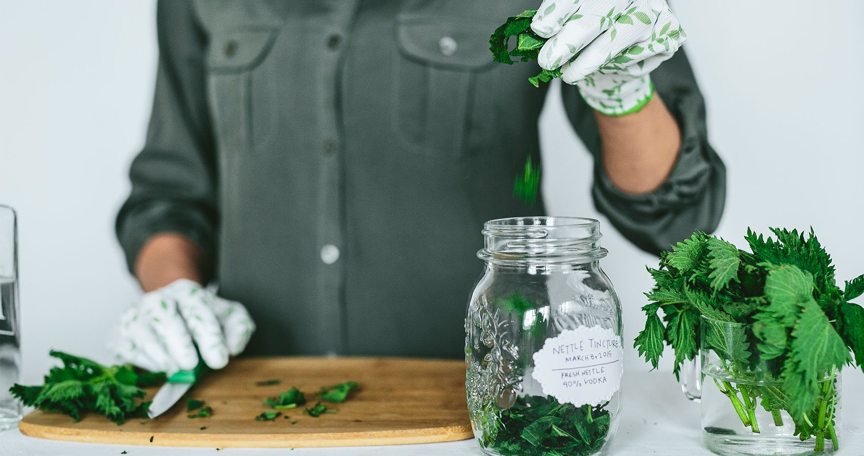 gloved hands putting herbs in jar